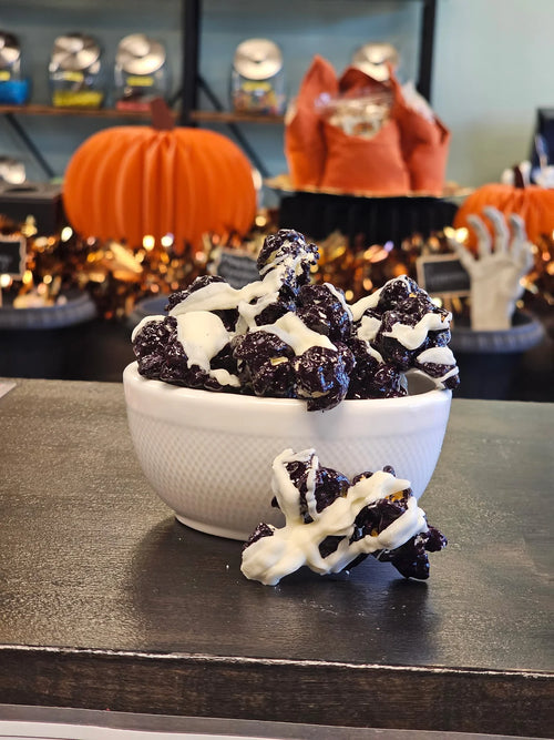 Bloody Fangtastic black popcorn with white drizzle in a white bowl, with Halloween decorations in the background